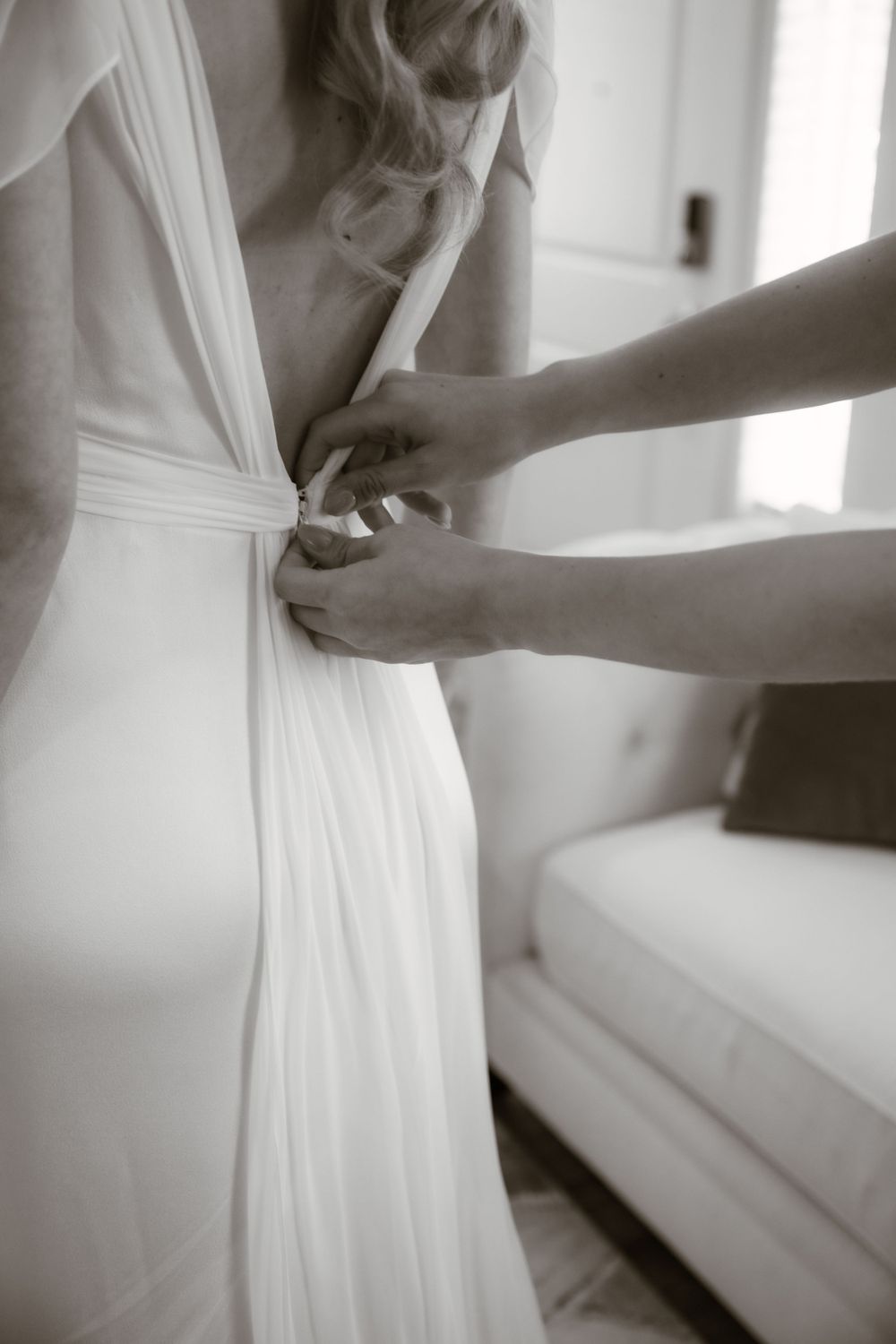 Close-up of hands adjusting the back of a white wedding gown in black and white.