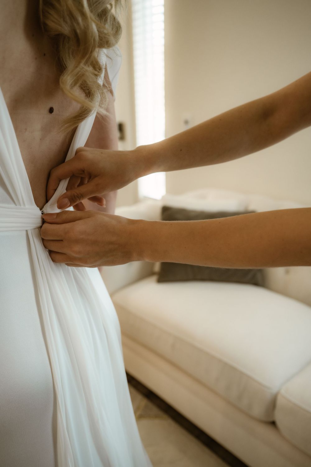 Detailed shot of hands securing the side of an elegant white wedding dress.