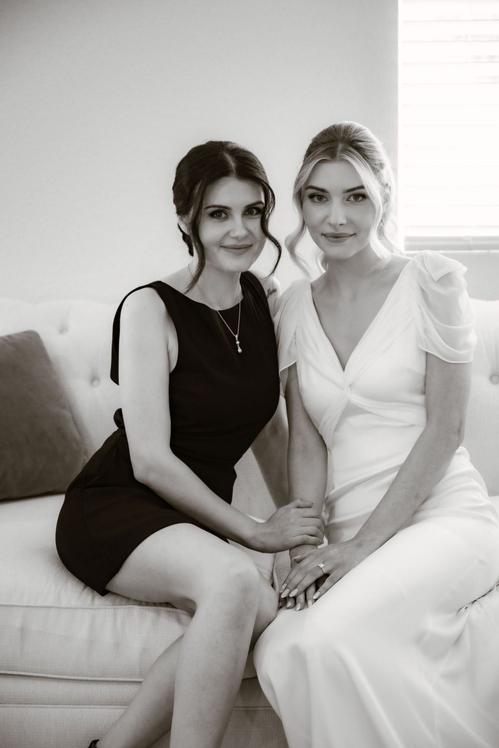 Two women sitting together on a white couch in black and white formal attire.