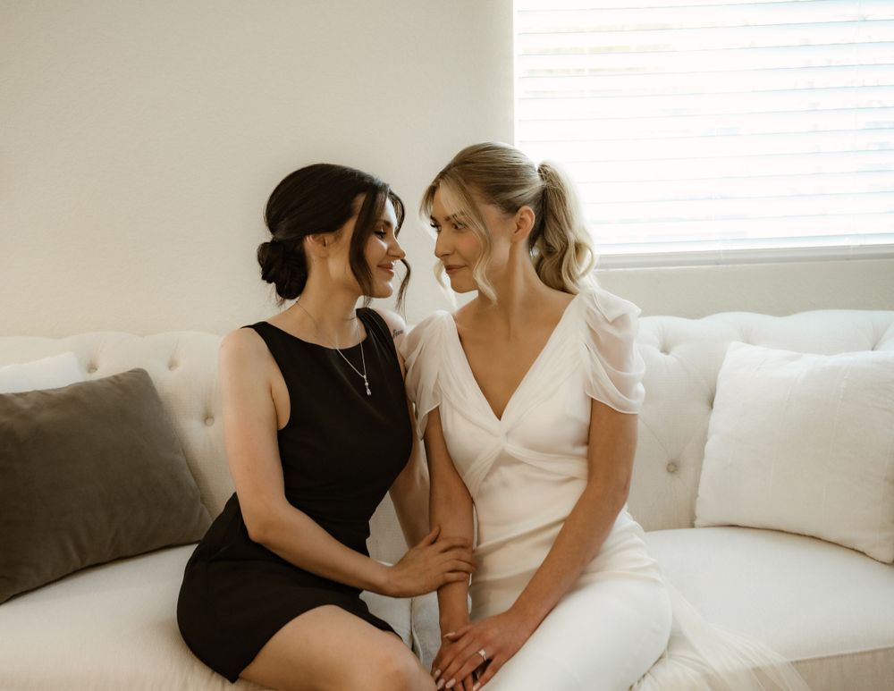 Two women in contrasting black and white dresses sharing a moment on a plush sofa.