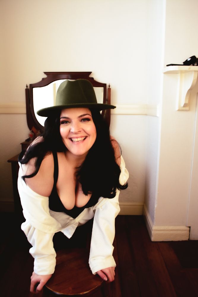 Boudoir style indoor portrait with hat and white shirt in natural light.