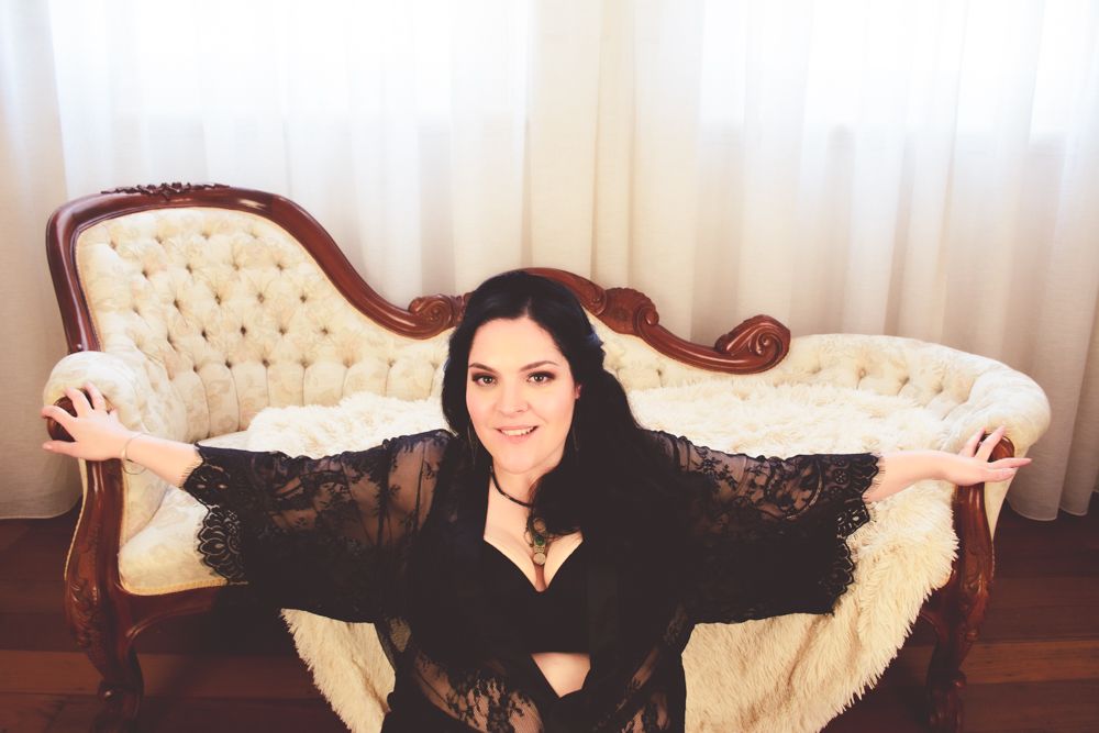 Elegant boudoir photo on vintage cream-colored chaise lounge wearing black lace.
