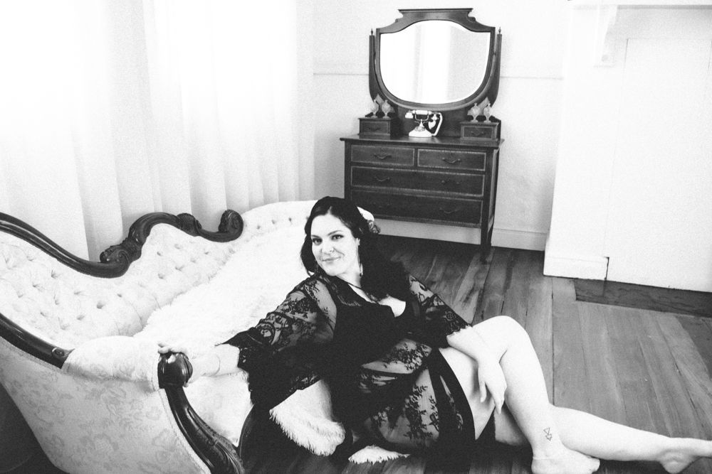 Black and white boudoir photo with vintage furniture and retro TV in background.