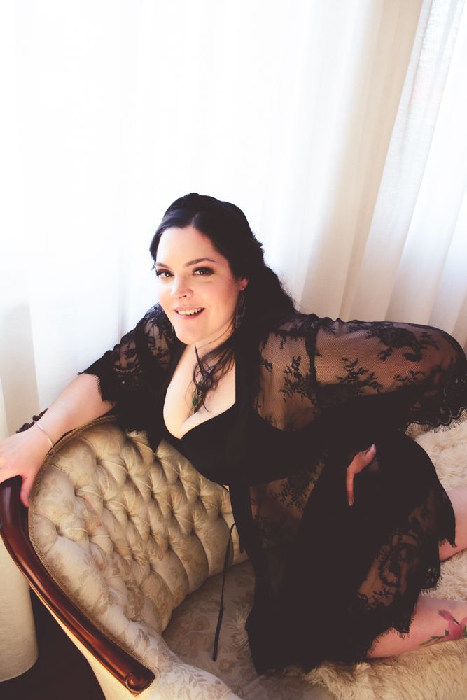 Romantic portrait on antique chair wearing black lace dress in soft lighting.
