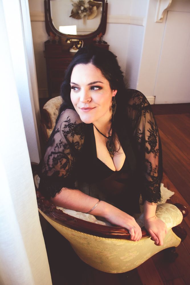 Intimate portrait seated in vintage chair wearing black lace by window light.