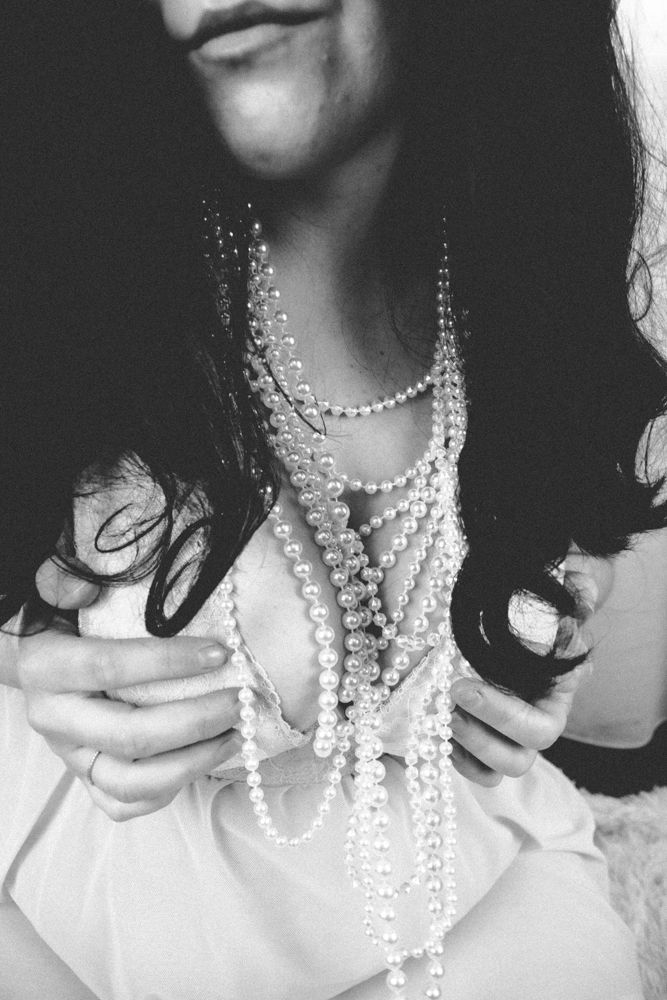 Dramatic black and white close-up of layered pearl necklaces against white fabric.