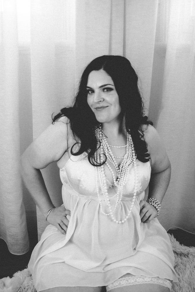 Vintage-inspired portrait with multiple pearl necklaces and white dress against light curtains.