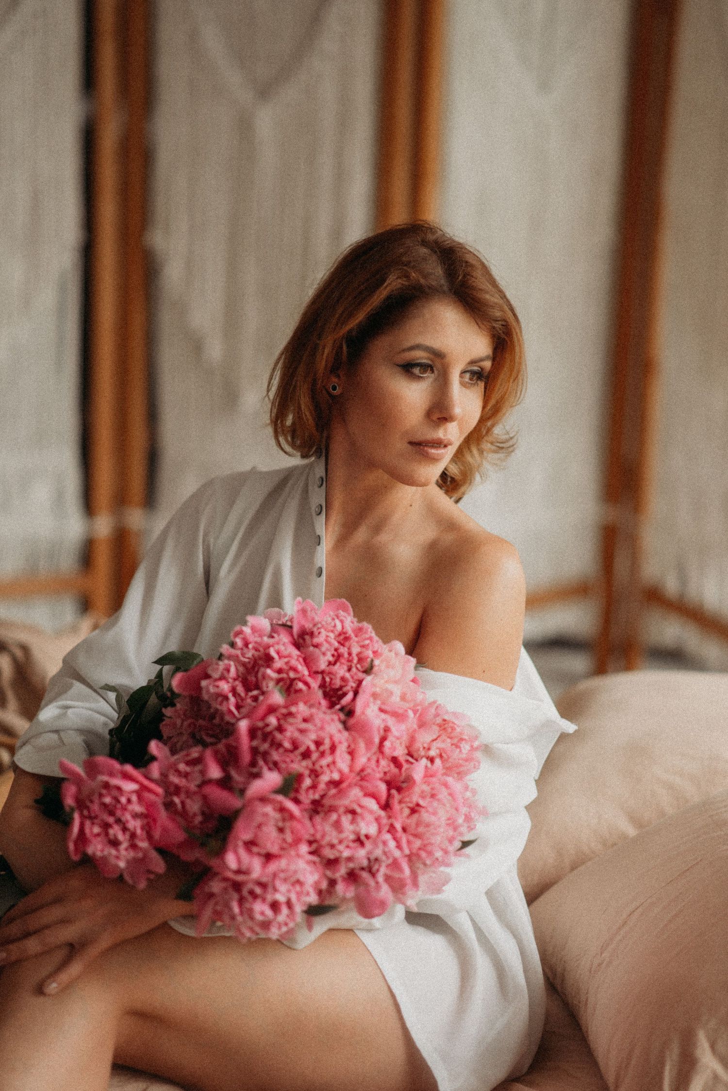 Romantic boudoir photography with pink peonies and white bedding.