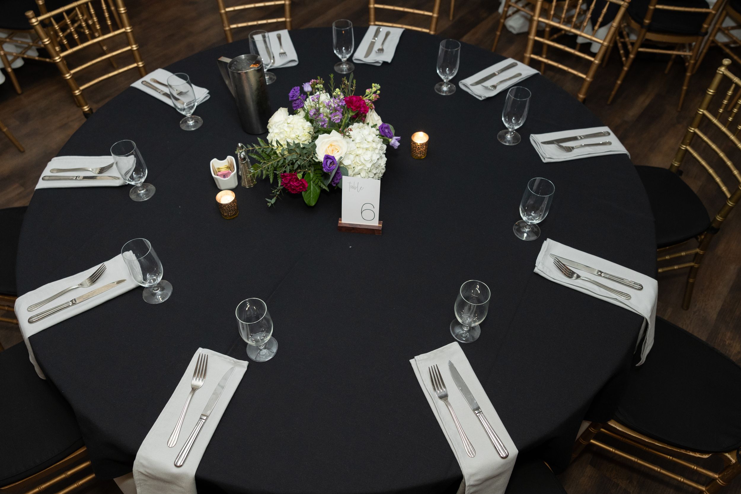 Elegant round dining table with black tablecloth and white place settings featuring a floral centerpiece.