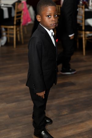 Young attendee in formal black suit stands attentively at event.