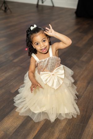 Young attendee in sparkly cream tulle dress poses playfully at formal event.