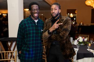 Two guests at a formal event pose together, one wearing a plaid shirt and another in a patterned blazer.