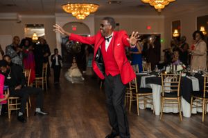 Person in red suit jacket dancing energetically at formal reception venue.
