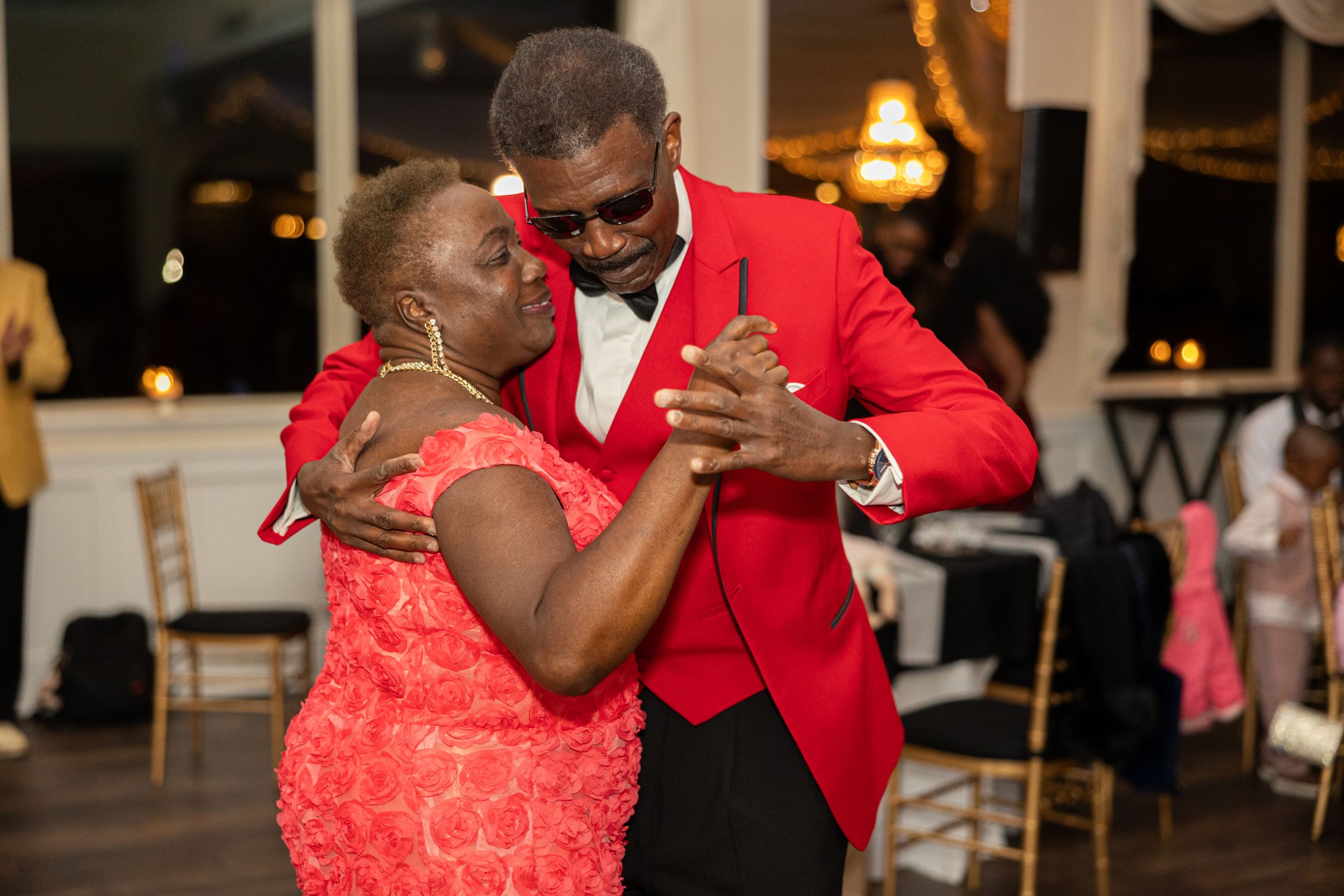 Dancing couple at formal event with one person wearing bright red jacket and other in coral dress.