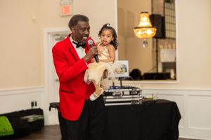 Person in bright red suit jacket holding small child at formal event.