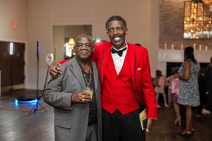 Two guests at formal event posing together, one in red blazer and another in grey suit.