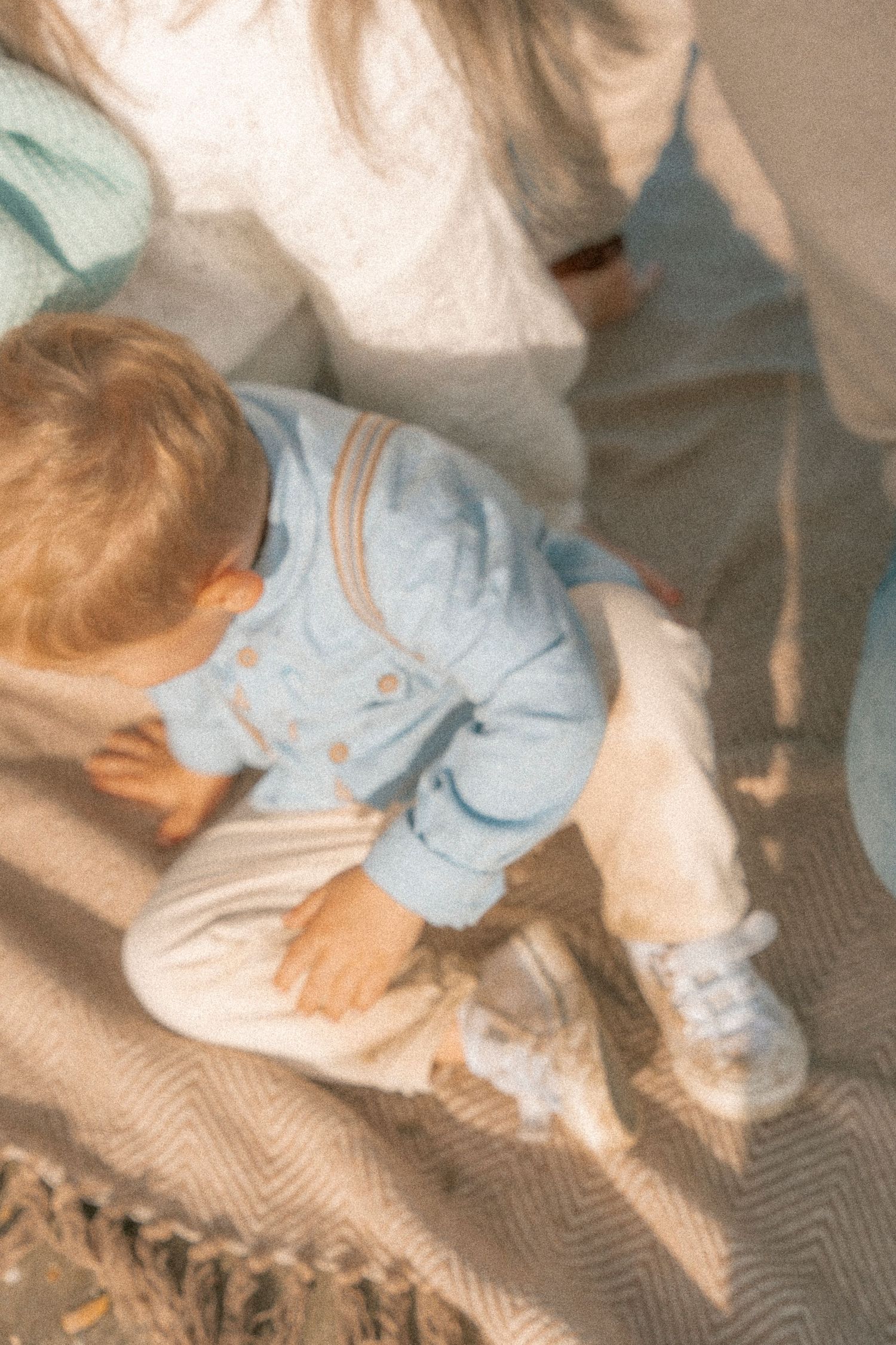 Candid moment of child in light blue outfit sitting on textured blanket.