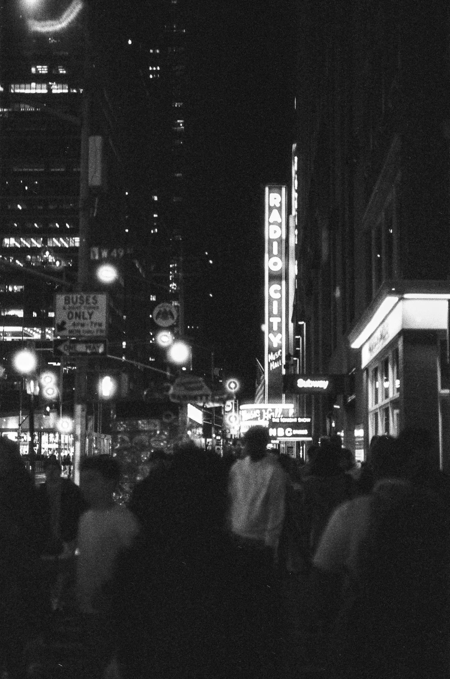 Nighttime city street with neon signs and blurred crowds of people walking.