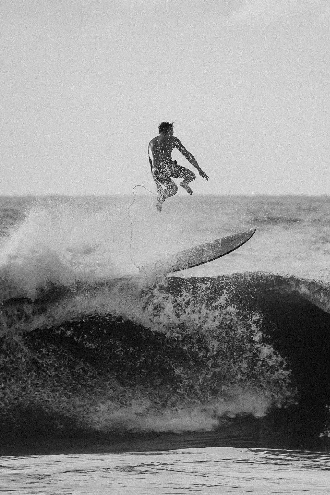 A surfer performs an aerial maneuver off a large wave in a dramatic black and white sequence of action shots.