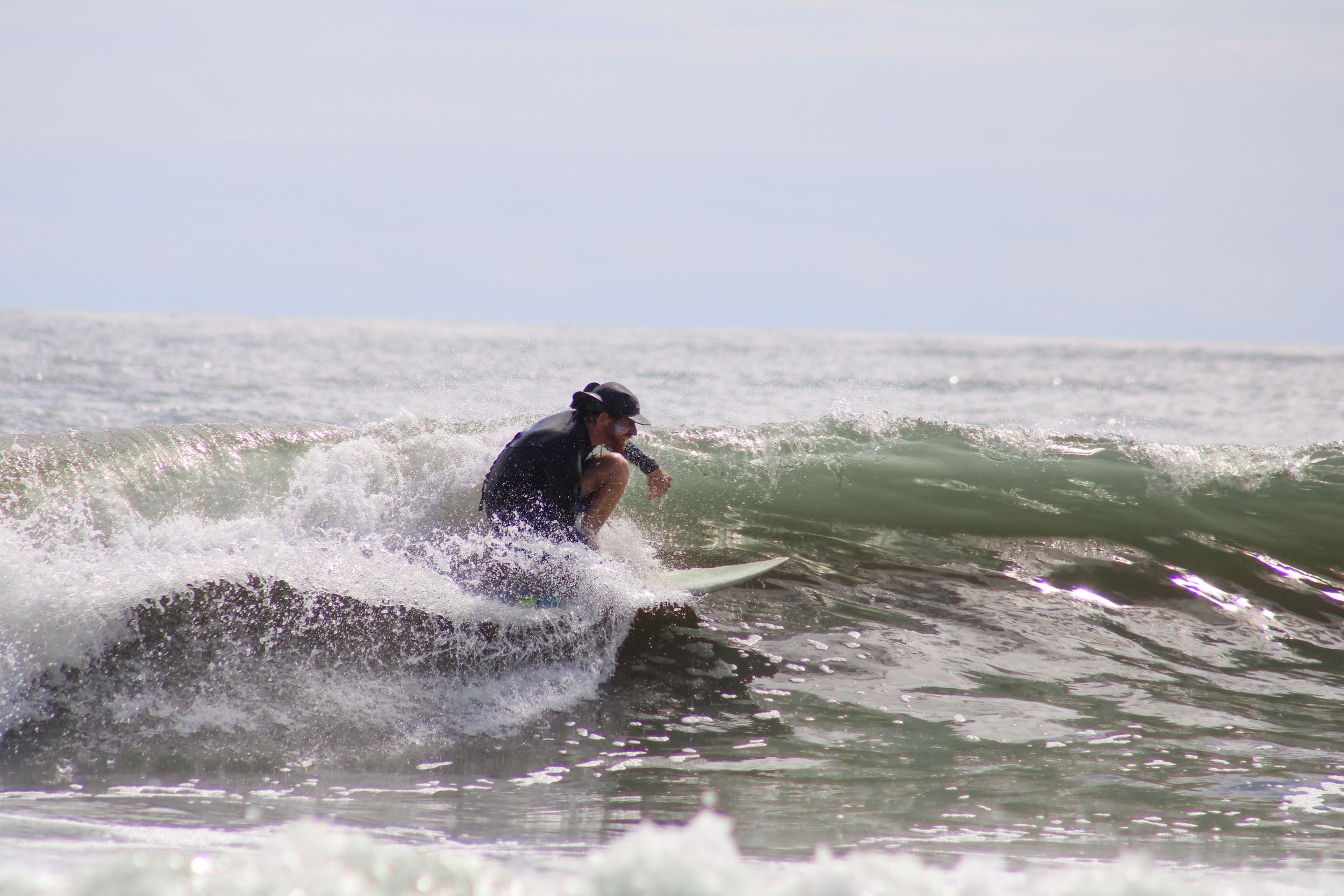 Surfer riding a green wave through ocean spray during overcast conditions.