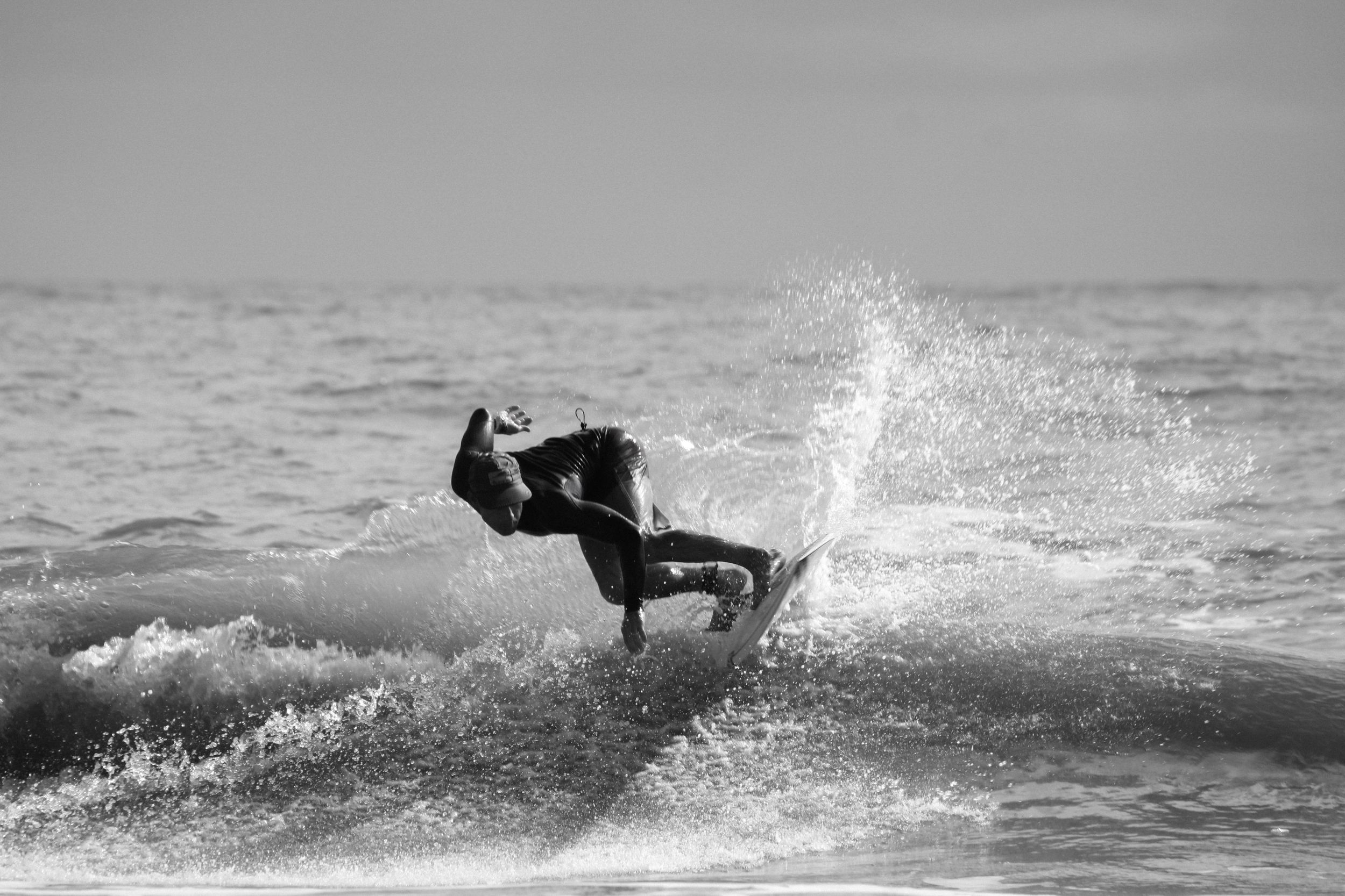 A black and white photo of a surfer executing an aerial trick above the waves.
