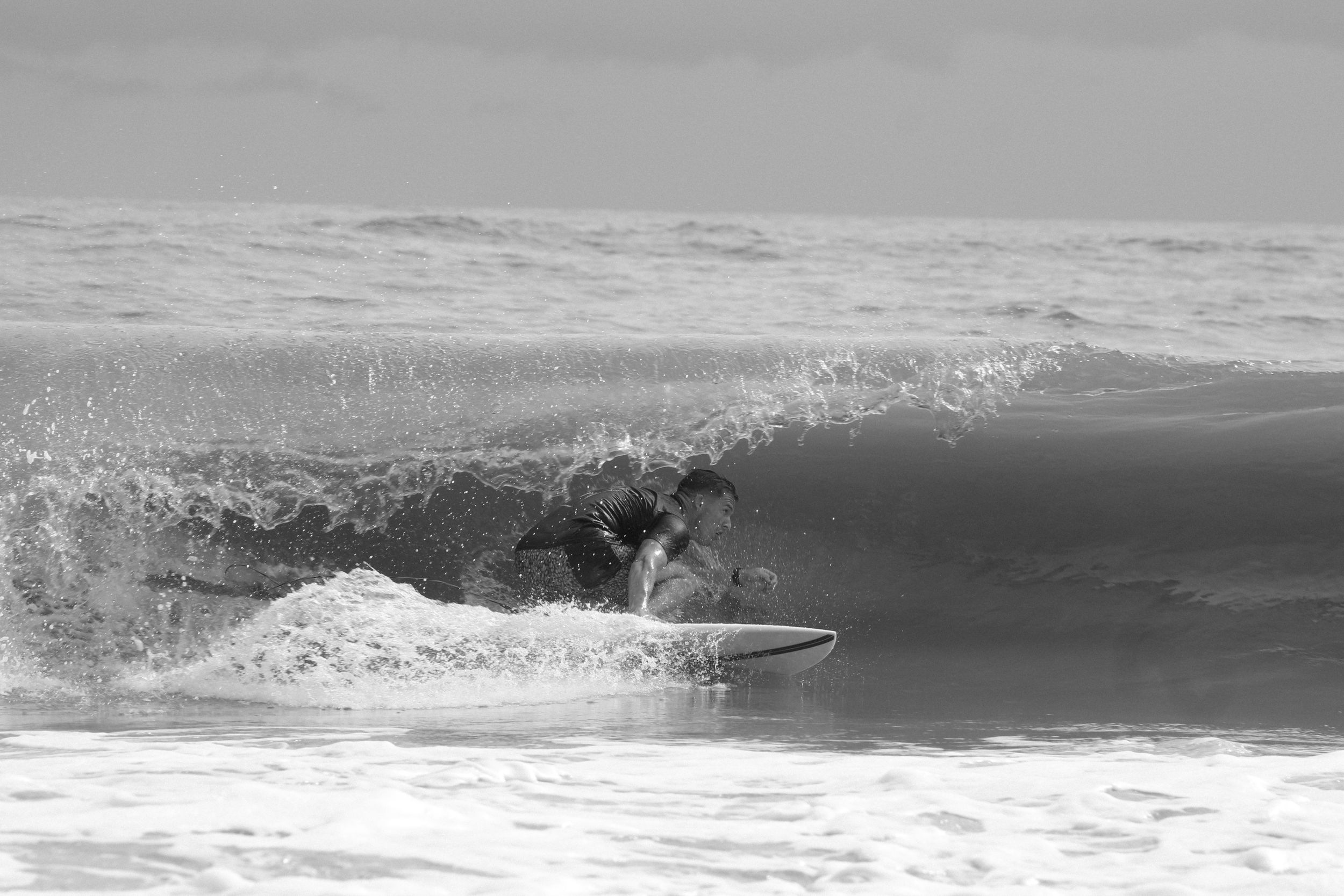 A black and white capture of a surfer navigating through a hollow wave.