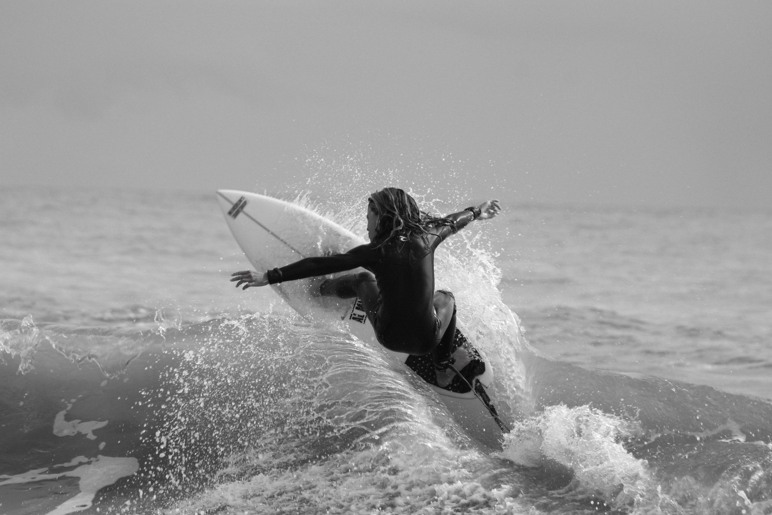 A black and white photo shows a surfer executing a powerful turn in the spray.