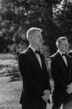 Two gentlemen in classic black tuxedos stand outdoors in natural lighting.