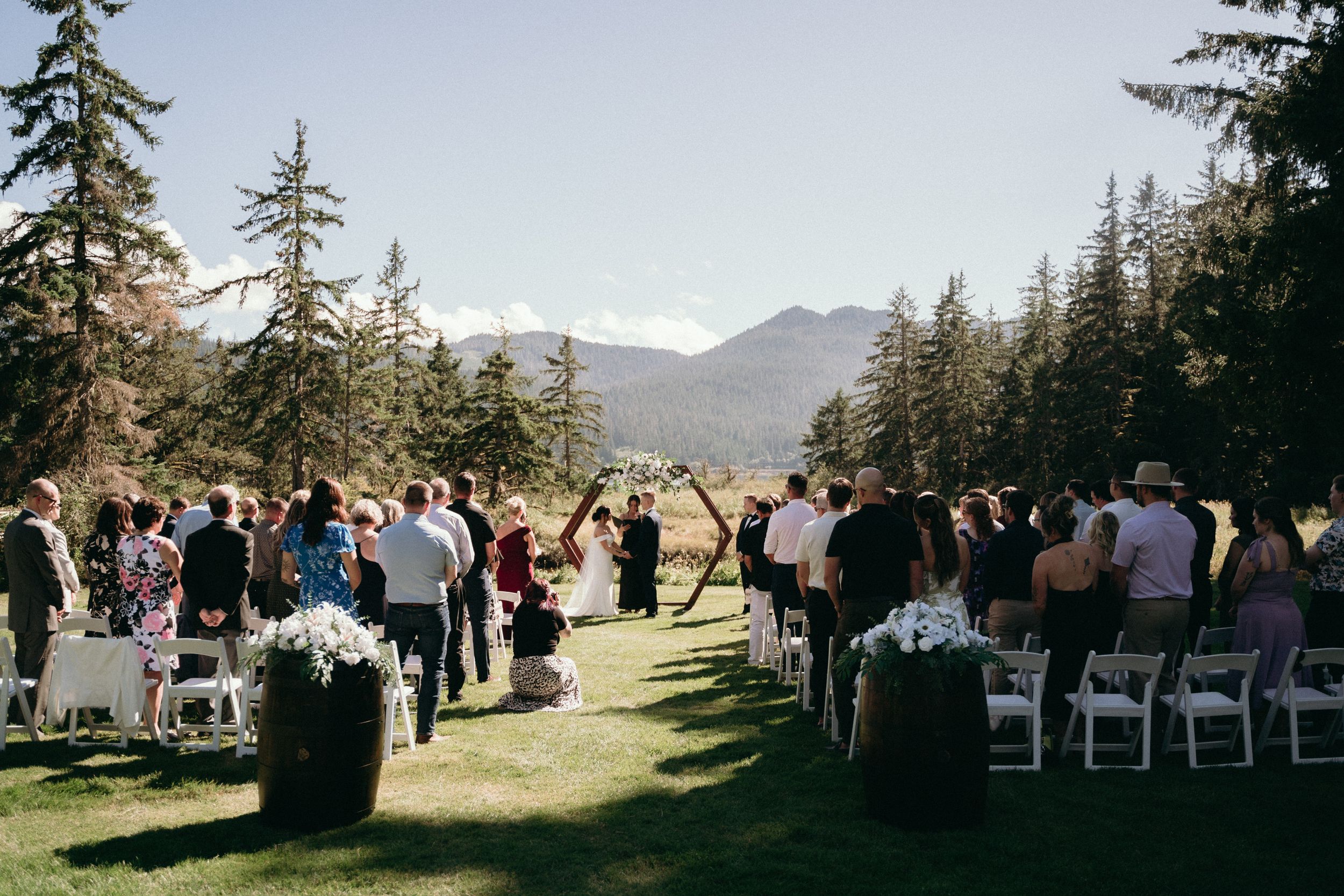An outdoor wedding ceremony setup with white chairs and mountain views in the background.