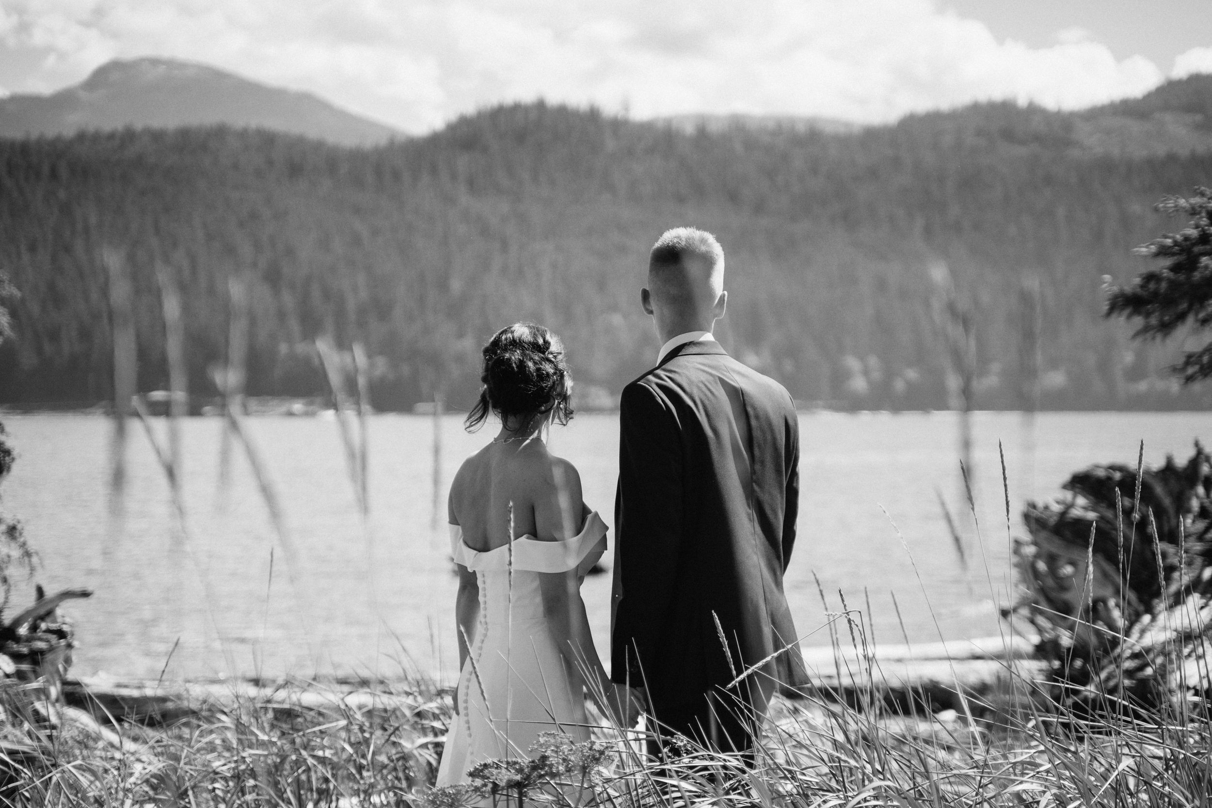 A couple stands overlooking a scenic mountain lake view in black and white.