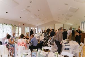 An elegant wedding reception venue with white decor, floral arrangements, and guests seated at round tables.