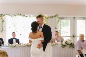 A romantic first dance moment at a wedding reception with floral garland decor and white tablescapes.