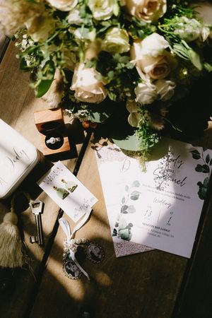 Wedding stationery and white roses arranged on wooden surface with dramatic lighting.