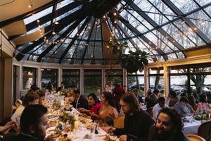 Wedding reception dinner in a glass-ceiling conservatory filled with guests enjoying their meal.