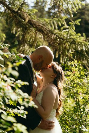 Newlyweds sharing intimate wedding day kiss in lush green forest setting.