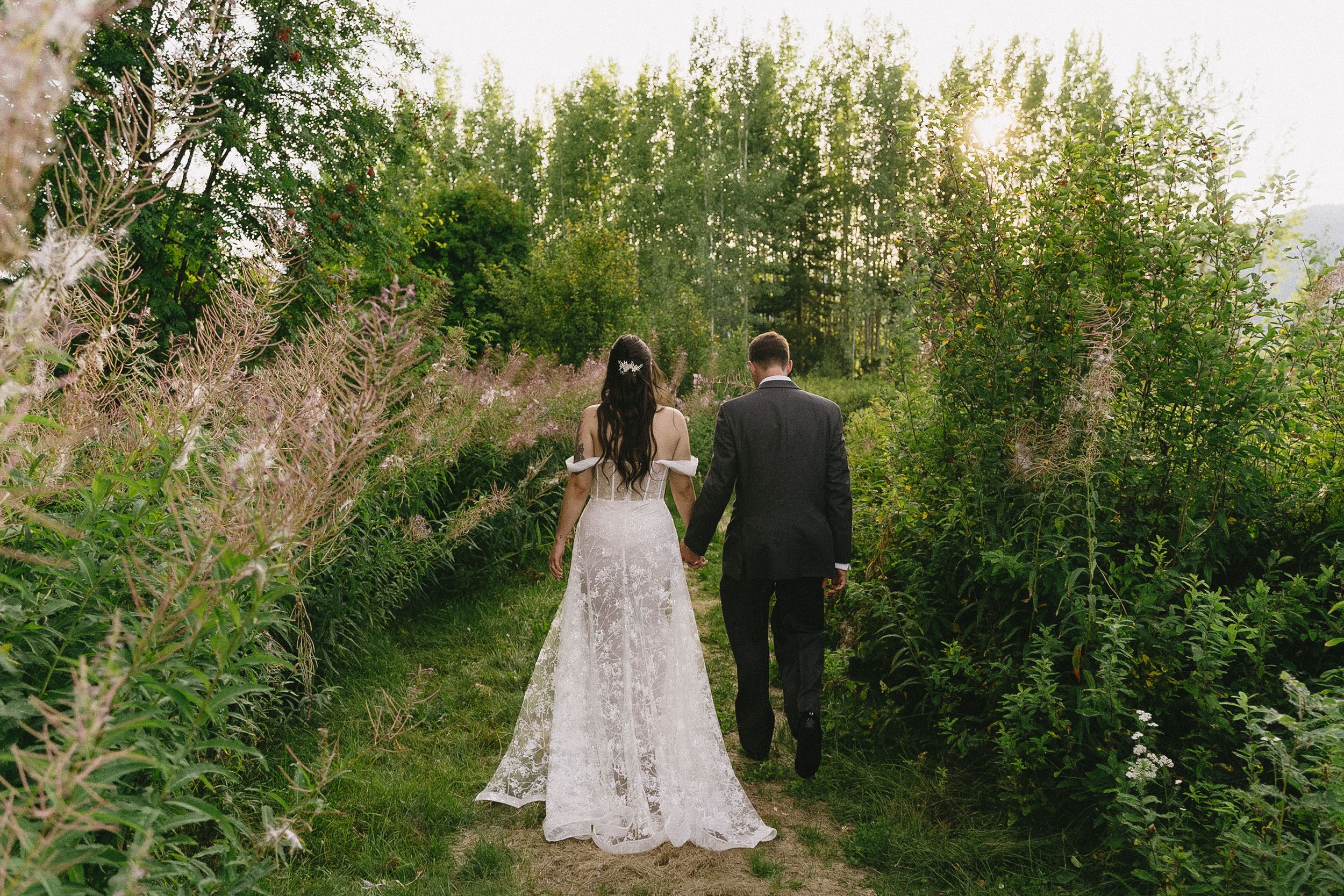 Newlyweds walk along a garden path surrounded by lush greenery and wildflowers.