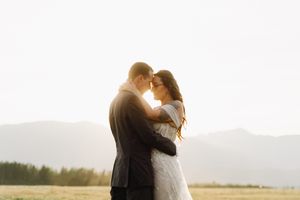 A romantic wedding couple embraces in golden sunlight with mountains in the background.