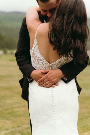 Close-up detail of a lace wedding dress back as couple shares an intimate moment.