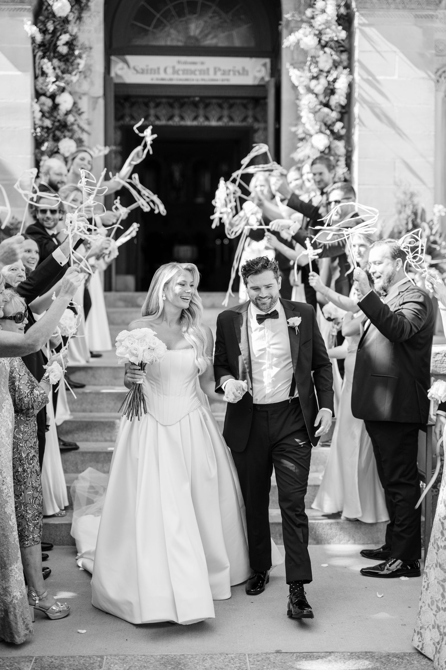 Black and white photo of a wedding ceremony inside an ornate cathedral with multiple couples in bridal gowns and guests.