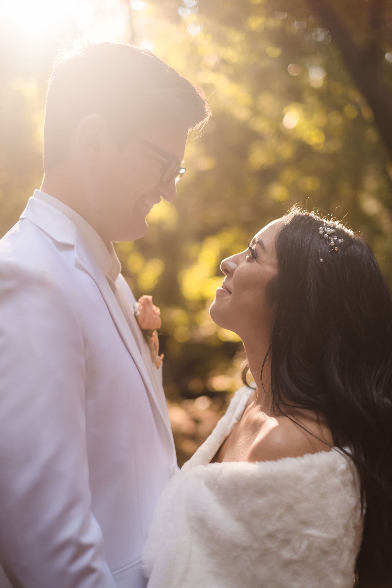 A romantic wedding couple shares an intimate moment in golden sunlight against a blurred natural backdrop. Santa Cruz redwood wedding