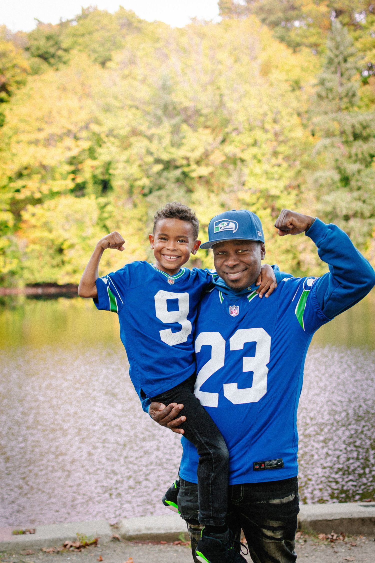 Father and son wearing Seahawks jerseys during a fall family photo session at Lake Fenwick Park.