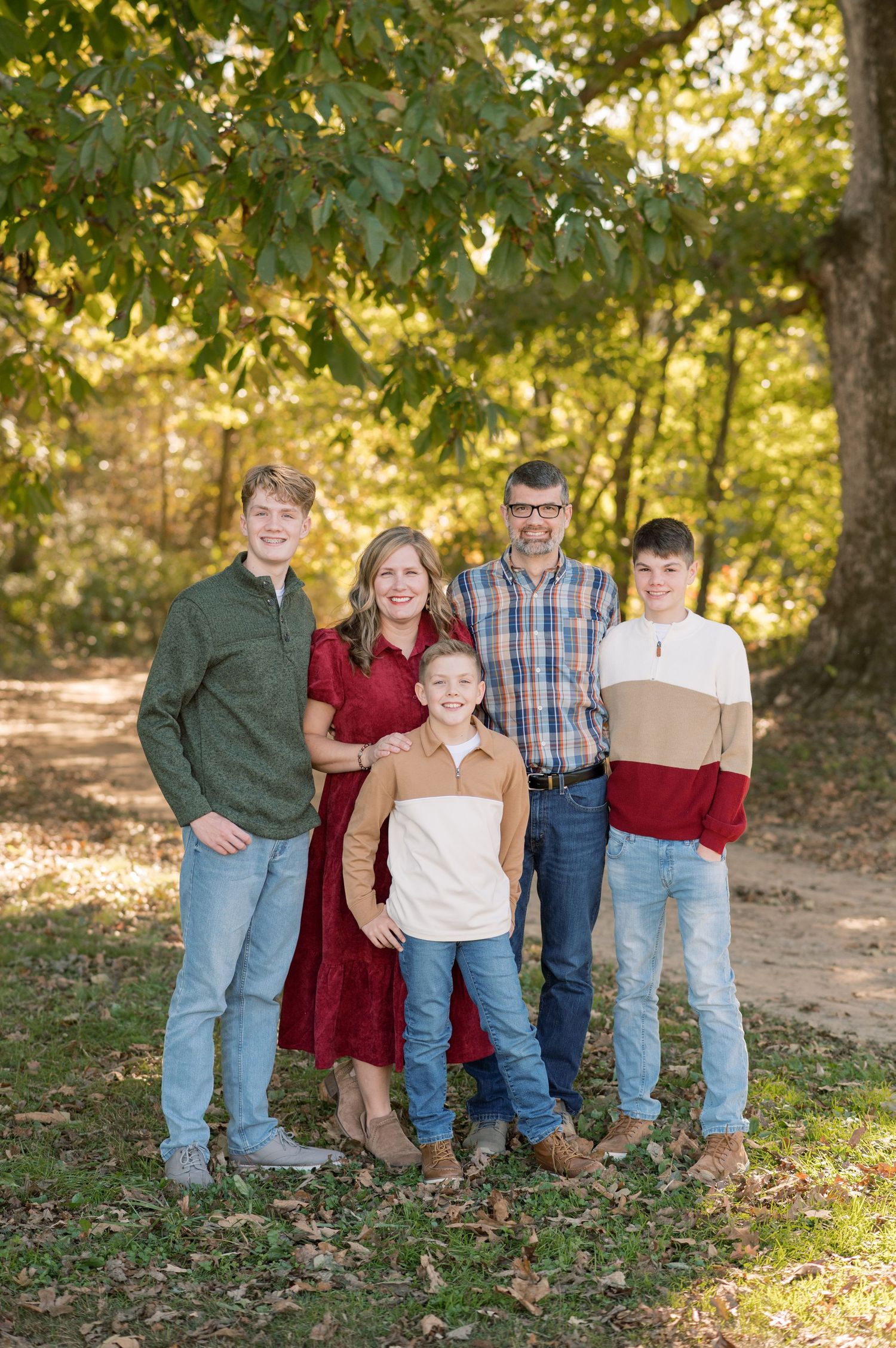 Multi-generational family in casual clothing posing together on fallen autumn leaves.