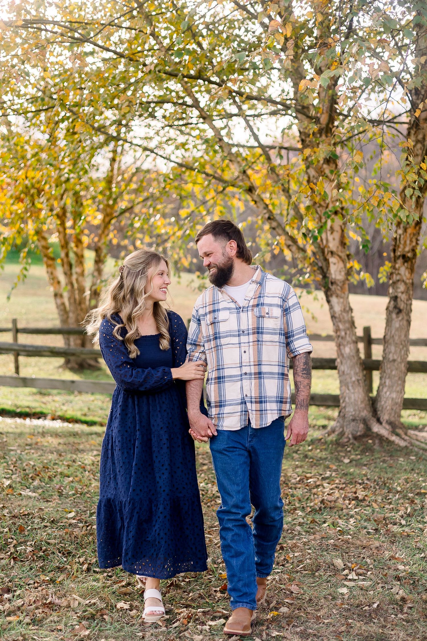 Couple laughing together during autumn photoshoot in wooded area with golden leaves and trees.