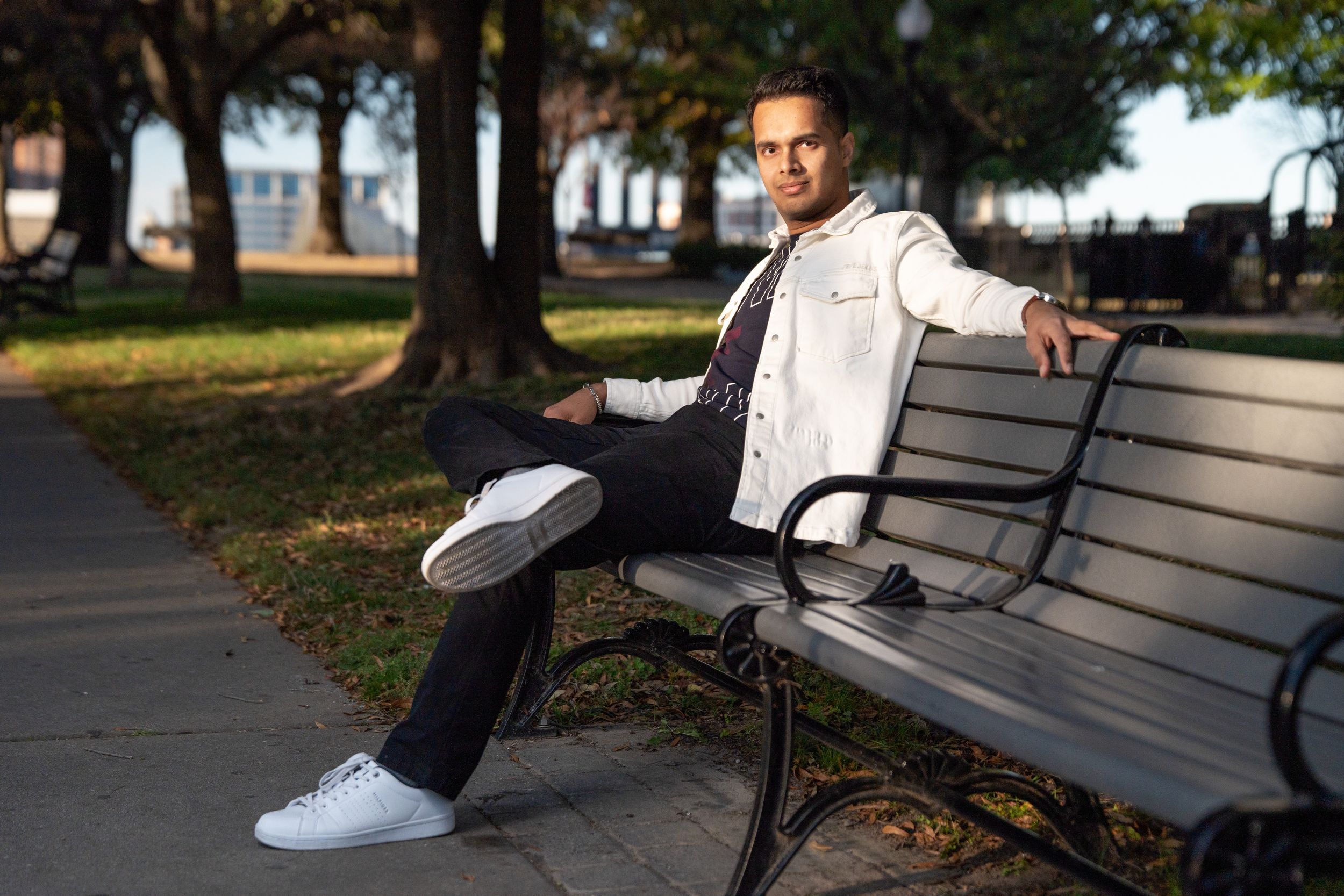 Person in white sneakers and black pants sits on wooden park bench in autumn setting.