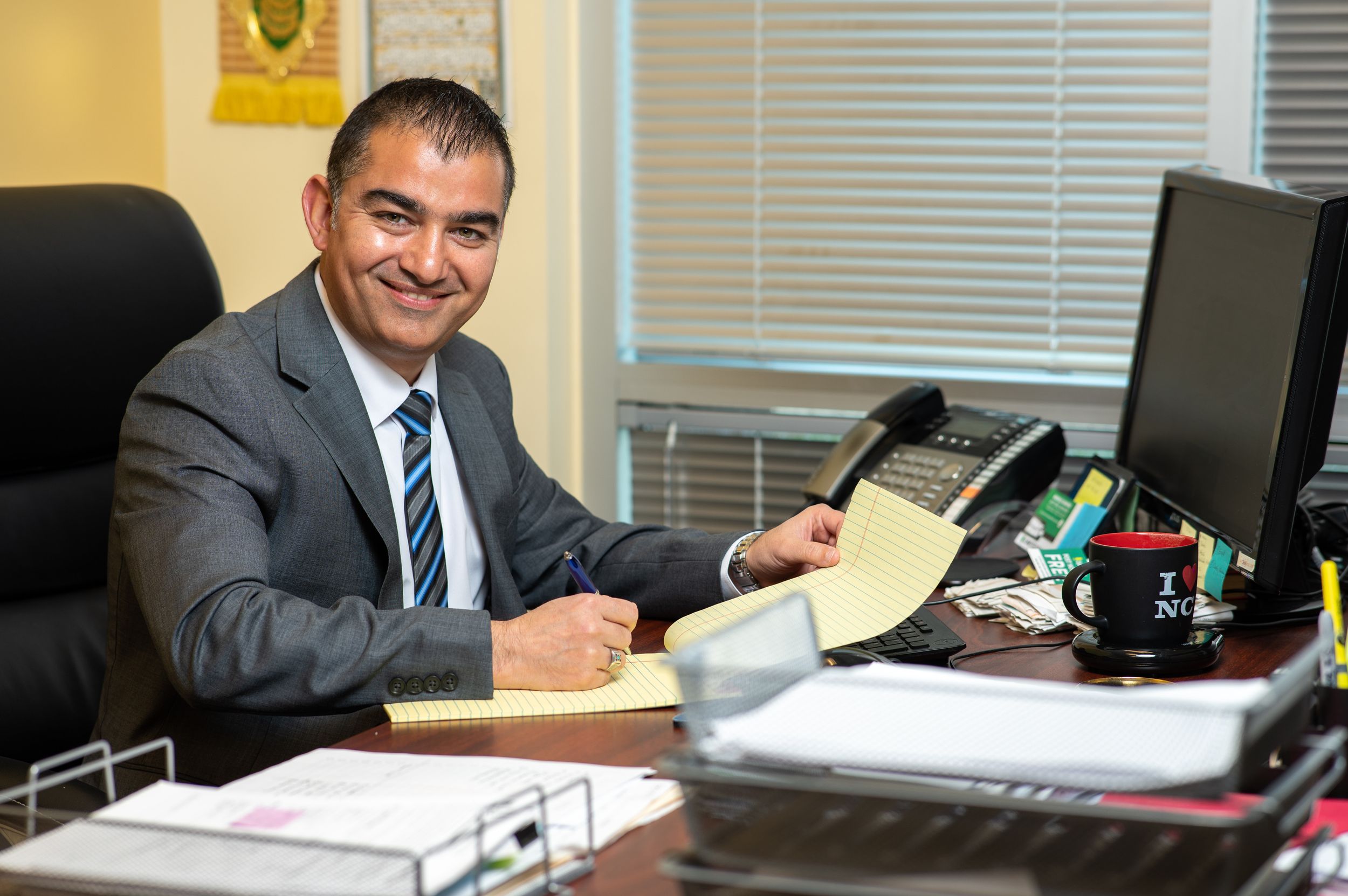 Business professional in suit works at desk with multiple computer monitors and office supplies.