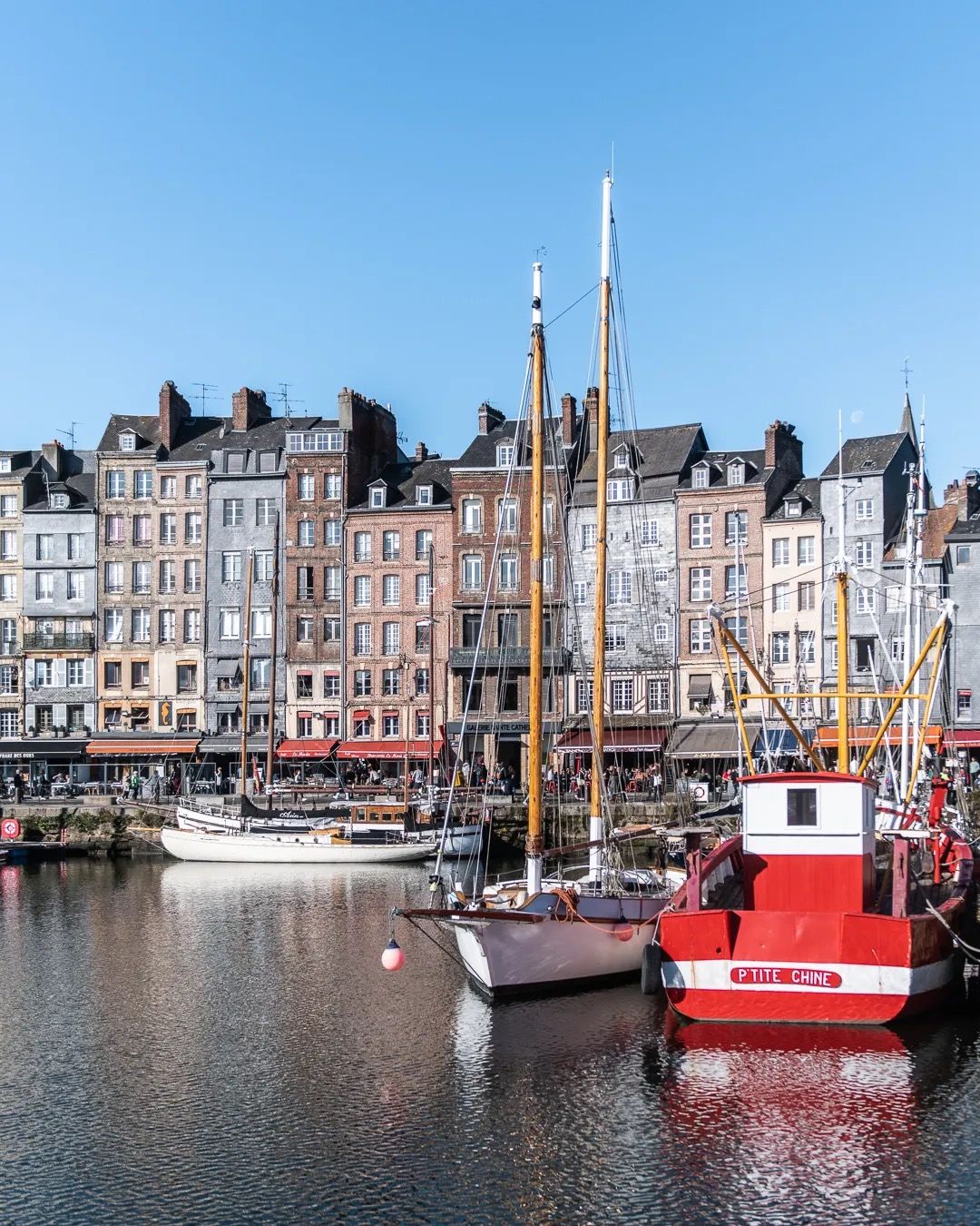 Harbour scene with moored boats and pastel-coloured houses reflecting in the water.