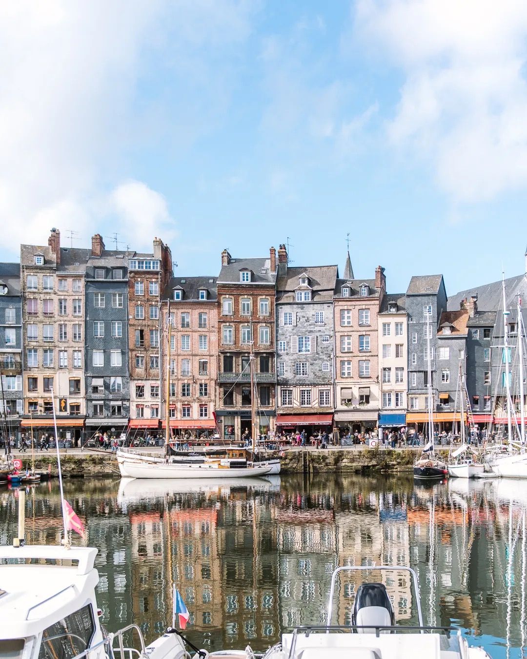 Colourful harbour buildings reflected in still water under a bright blue sky.