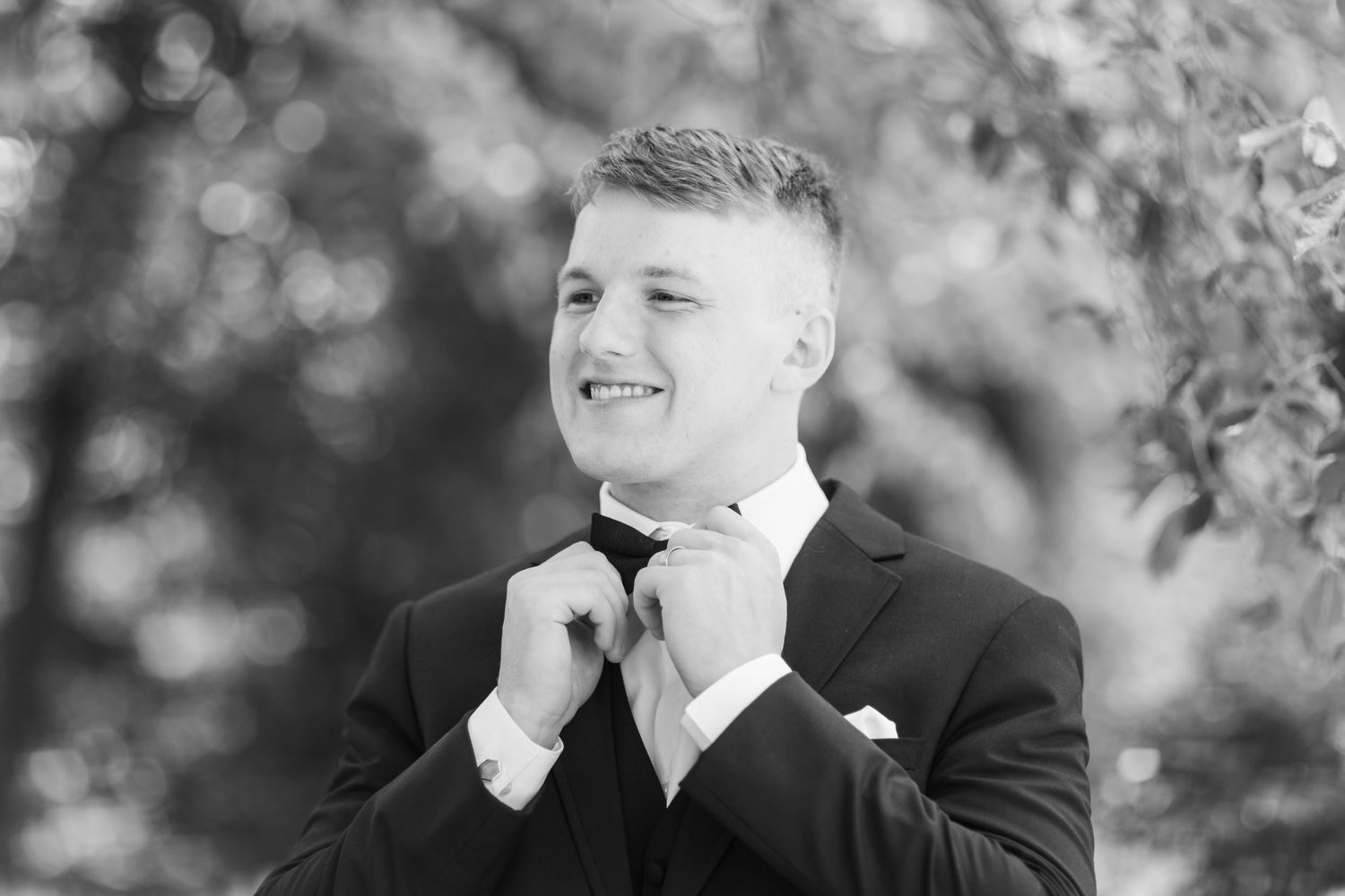 Black and white portrait photo showing a joyful expression and laughter against a soft blurred outdoor background.