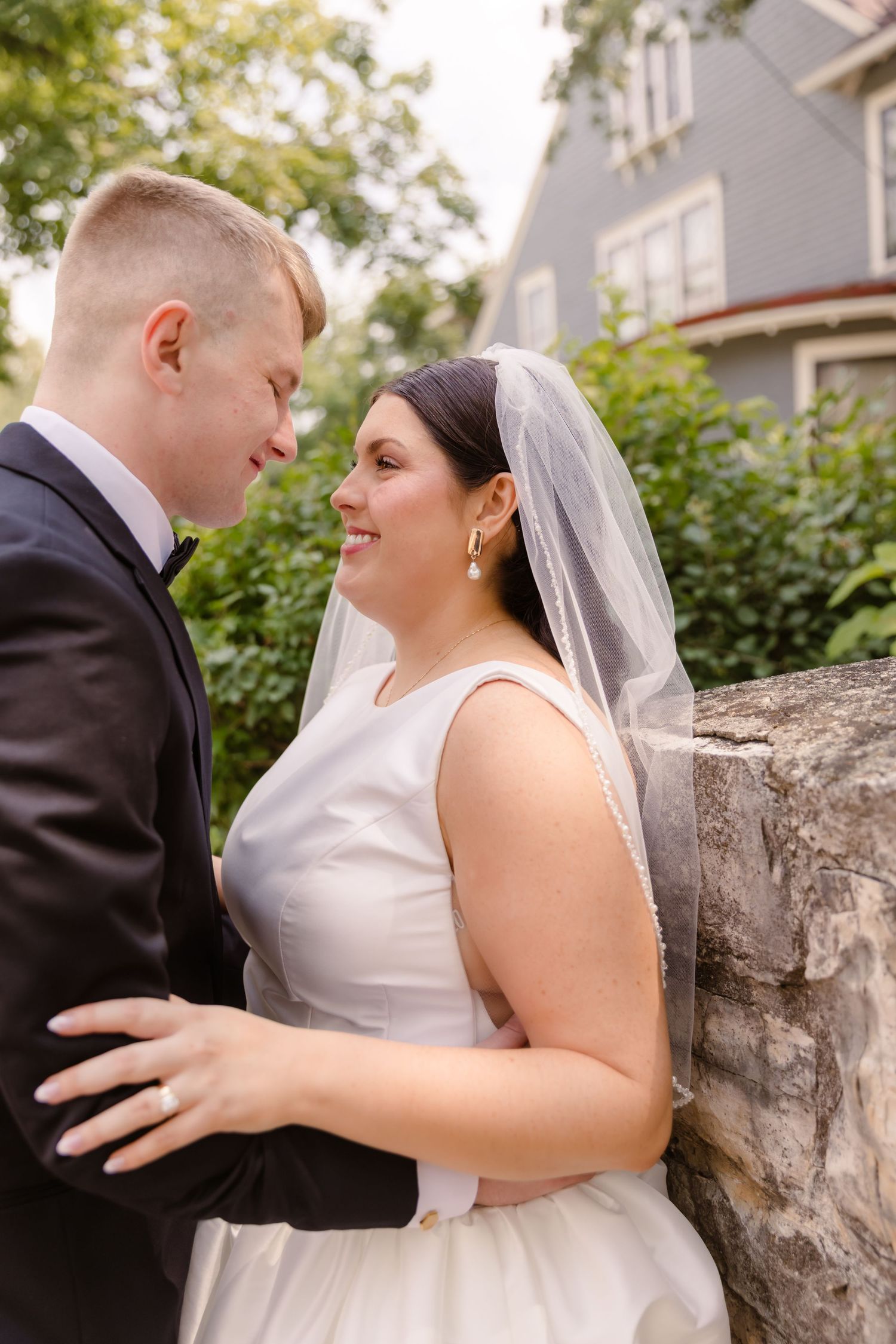 Bride and groom share intimate moments against a stone wall during their outdoor wedding photo session.