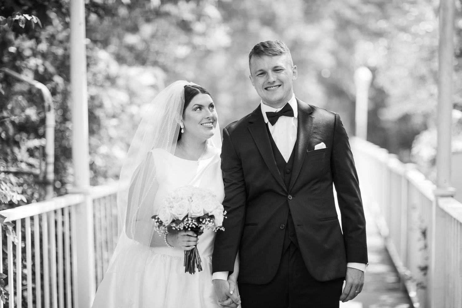A black and white wedding photo showing a couple walking together on an outdoor porch with white railings.